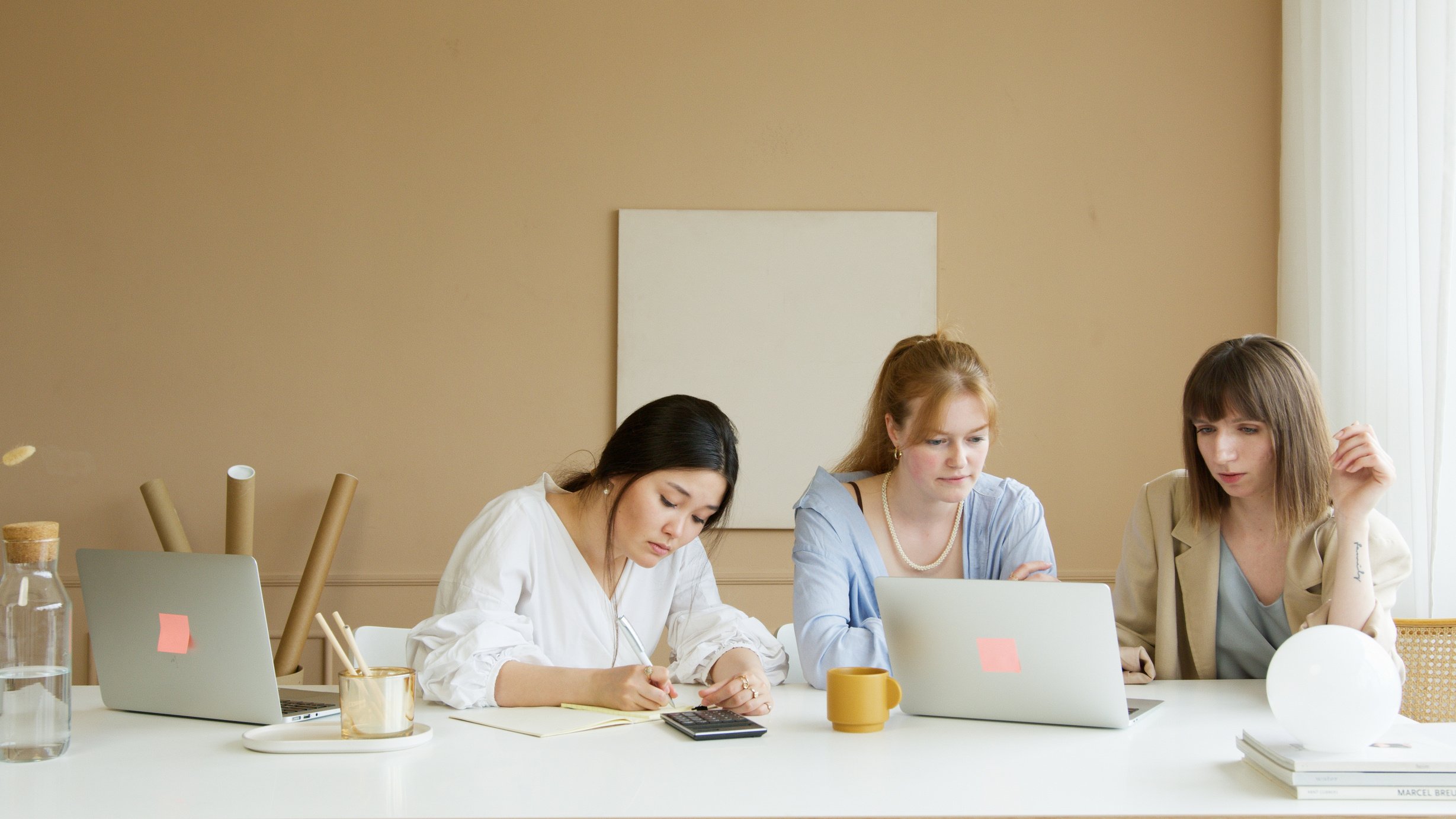 2 Women Sitting at Table Using Macbook